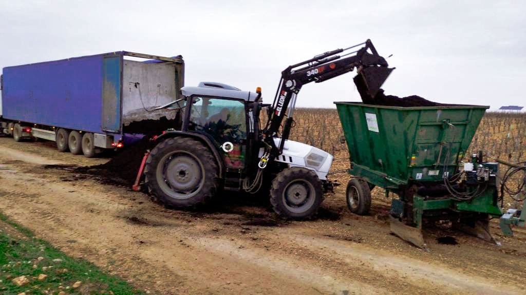 Tractor vertiendo abono en tolva para abonado de fondo de cultivo de pistachos.