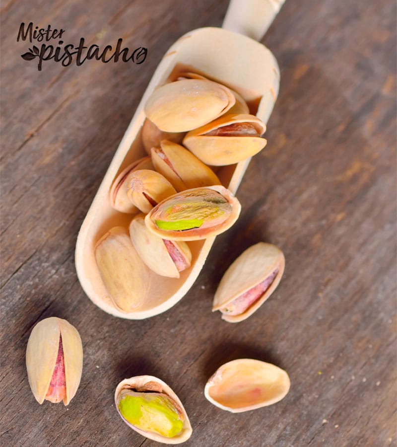 Spoon of raw pistachios on an old wooden background.