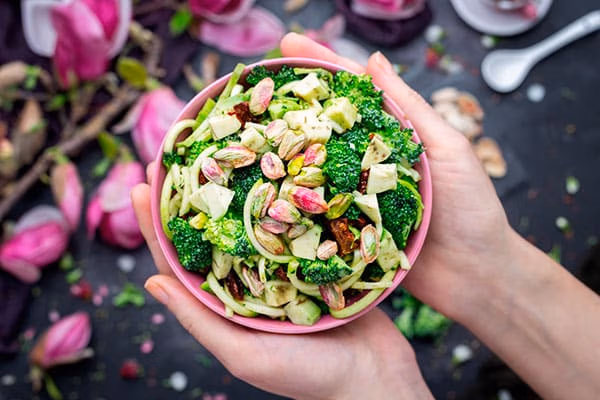 Immagine di una persona che tiene in mano una ciotola di insalata vegana con pistacchi.